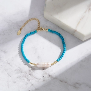 Handmade turquoise beaded bracelet with baroque pearl and gold chain on marble base