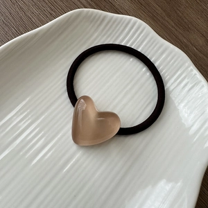 Detail of amber resin heart pendant on elastic hair tie resting on ceramic tray
