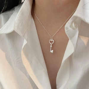 Close-up of 925 sterling silver heart-shaped key necklace on a model wearing a white shirt