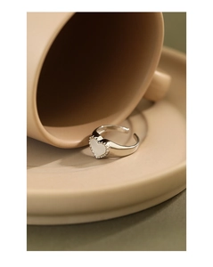 Detailed close-up of a silver heart-shaped ring with white shell inlay on a saucer