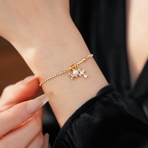 Détail d'un bracelet doré élégant avec une perle blanche et un pendentif croix en cristal