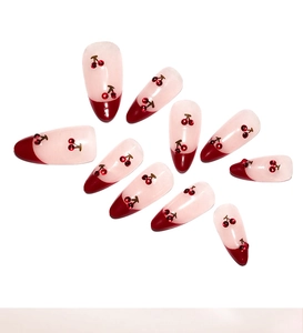 Detail of almond-shaped press-on nails with red French tips and 3D cherry patterns