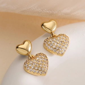 Elegant gold heart earrings with zircon studs and drop pendants on soft fabric
