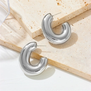 Polished silver stainless steel large G-shaped hollow hoop earrings on stone background