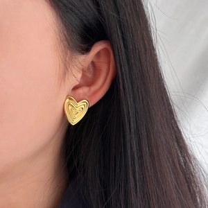 Close-up of a model wearing a textured golden heart earring in a stylish vintage design
