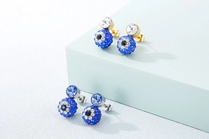 Close-up of gold and silver devil eye stud earrings with blue crystals on display