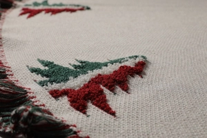 Detailed macro shot of white knitted Christmas tree skirt with festive red and green pine trees