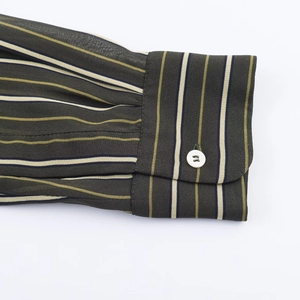 Detail of shirt cuff featuring multi-color stripes and white button on olive fabric
