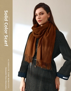 Detail of brown solid color scarf with tassels worn over a green plaid coat