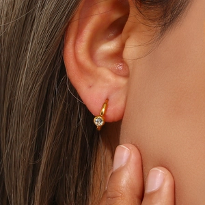 Detail of 18K gold plated hoop earring with a sparkling round zircon worn by a model