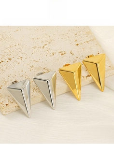 Macro detail of geometric 18K gold and silver pyramid stud earrings on a stone tray