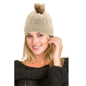 Detail of chunky cable knit beanie in cream white with a fluffy faux fur pompom decoration