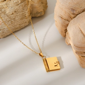 Close-up of heart-engraved gold book locket pendant on a minimalist chain necklace