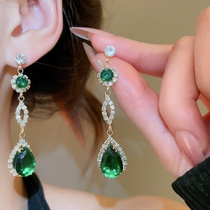 Macro detail of dark green teardrop drop earrings with gold metal and white zircon stones