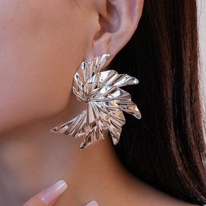 Close-up of a model wearing large silver spiral petal earrings with metallic luster