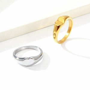 Polished gold and silver stainless steel heart signet rings on a white stone pedestal