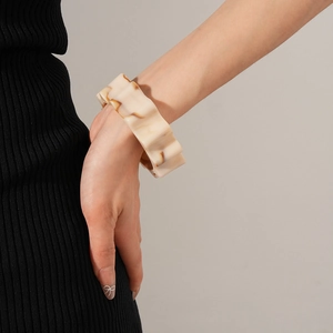 Detailed view of wide wave resin bangle in cream marble worn on a model's wrist