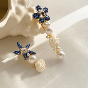 Gros plan sur des barrettes étoile de mer dorées avec strass bleus et perles blanches