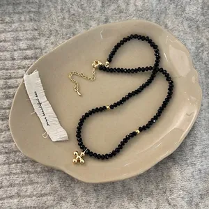 Close-up of black beaded necklace featuring a gold cross pendant and adjustable clasp