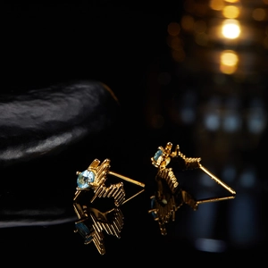 Macro shot of gold geometric earrings featuring round blue gemstones and 925 silver studs