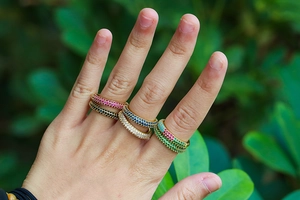 Hand model wearing five stacked micro-pave colorful zircon rings in outdoor setting
