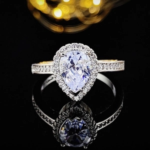 Macro shot of halo pear-cut purple gemstone ring with diamond pavé band on black mirror
