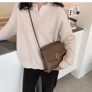 Vue détaillée du sac bandoulière marron foncé avec boucle dorée sur un fond minimaliste