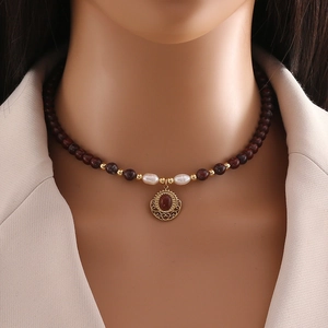 Detail of natural deep red beads and vintage gold pendant necklace on a female model