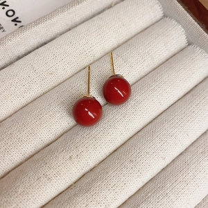 Macro detail of red bead stud earrings with gold plating on a beige fabric jewelry box