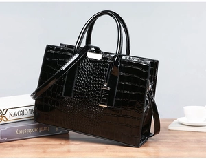 Detail of a black faux crocodile leather handbag with silver hardware on a wooden desk
