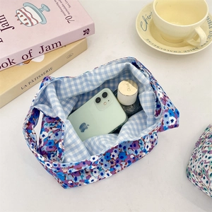 Close-up of floral corduroy wrist bag with blue checkered lining holding a phone and perfume