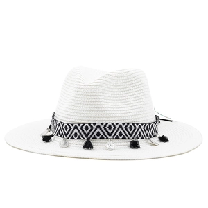 Détail d'un chapeau fedora blanc avec ruban ethnique et pièces métalliques suspendues