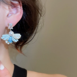 Macro detail of elegant fan-shaped pearl earrings with blue petals and zircon on a model