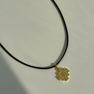 Detail of vintage gold medallion pendant on black cord necklace with textured relief