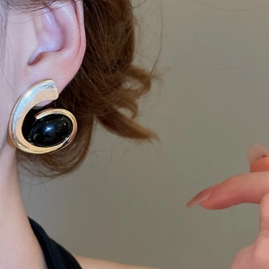 Detailed view of an oval black stone earring in a gold spiral metal setting on a model