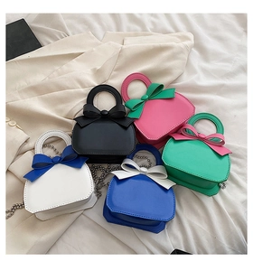 Detail of colorful mini handbags featuring ribbon bows and elegant metal chain straps