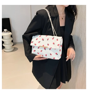 Détail du sac blanc à imprimé fraise avec chaîne dorée sur une tenue noire