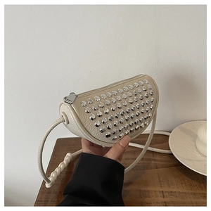 Detail of cream crescent crossbody bag featuring silver rivets and woven rope shoulder strap