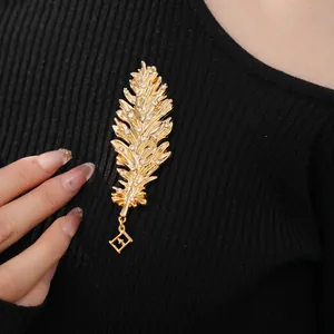 Elegant gold feather brooch with white rhinestones and square pendant on black knit