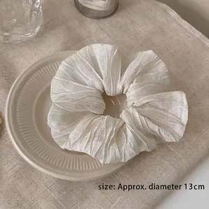 Detail shot of a white oversized ruffled scrunchie showing 13cm diameter on texture fabric