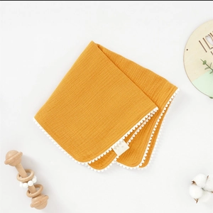 Détail de la serviette en mousseline jaune moutarde pour bébé avec bordure à pompons