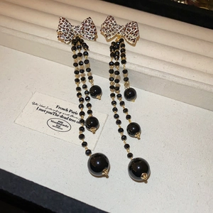 Close-up of leopard print bow earrings with black bead tassels and gold metal accents