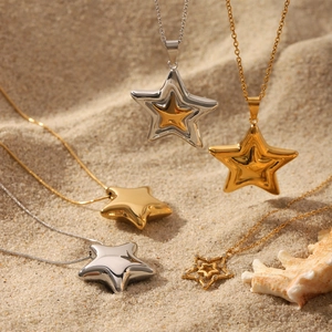 Five assorted gold and silver stainless steel star pendant necklaces on sandy beach