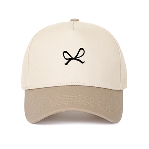 Detail of embroidered black bow on a beige and khaki panel trucker hat with stitching