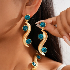 Macro detail of wave-shaped gold earrings with inlaid blue crystals on a female model