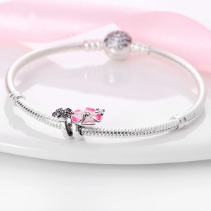 Detalle de pulsera de plata con dije de flor rosa y circón púrpura sobre una bandeja