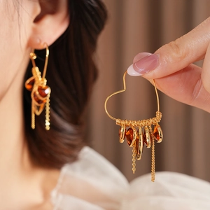 Detailed view of 18K gold-plated heart earrings with amber glass drops and metal tassels