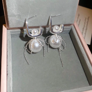 Macro detail of silver drop earrings with pearls and delicate tassel chains on velvet