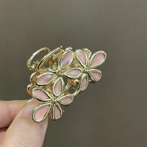 Detalle de una pinza para el pelo con flor rosa de metal y acabado dorado en mano