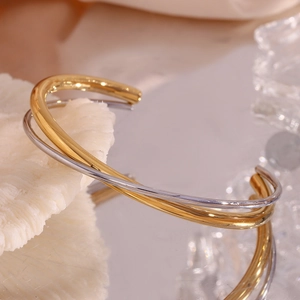 Macro shot of gold and silver minimalist double-layer crossover open cuff bracelets
